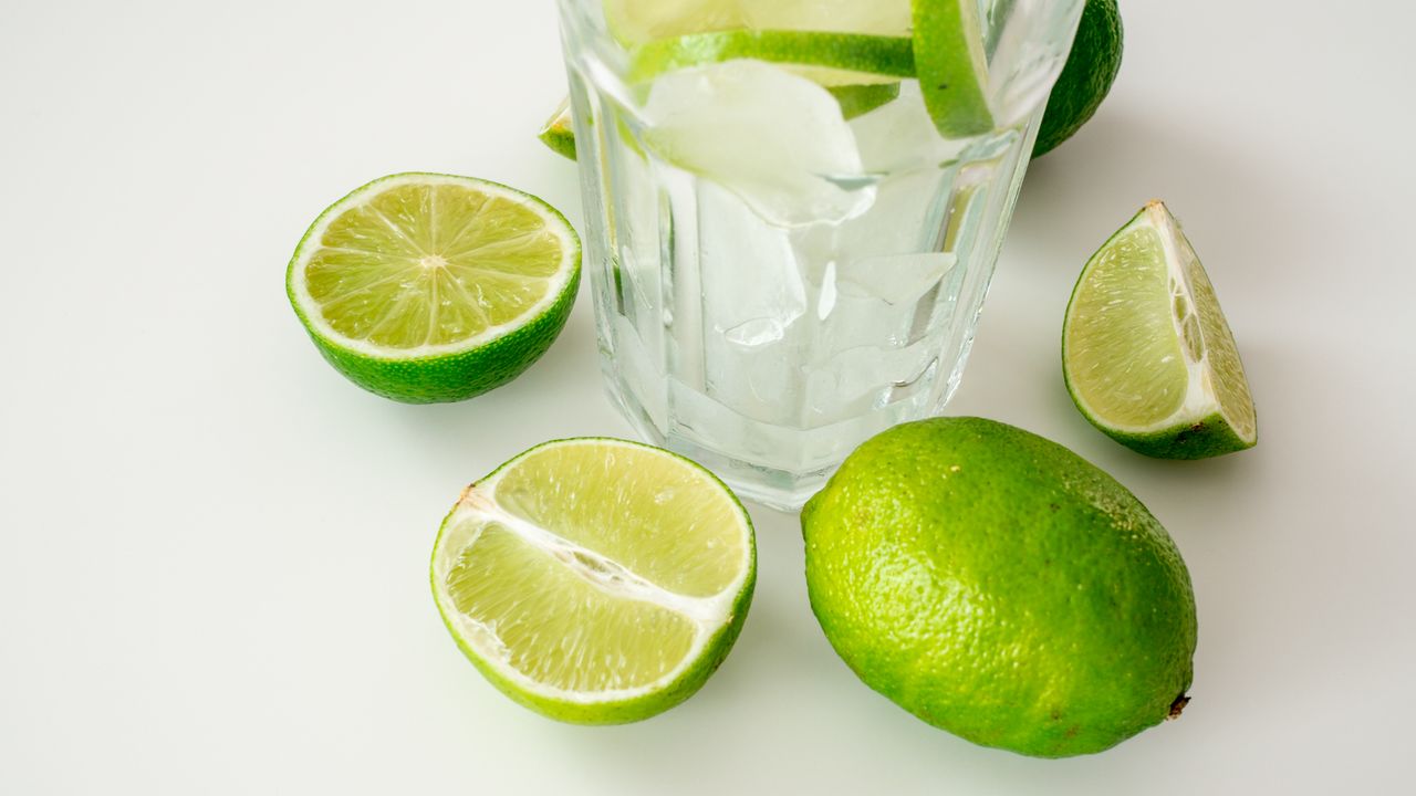 A crisp and refreshing glass of ice water with sliced limes on a bright surface.