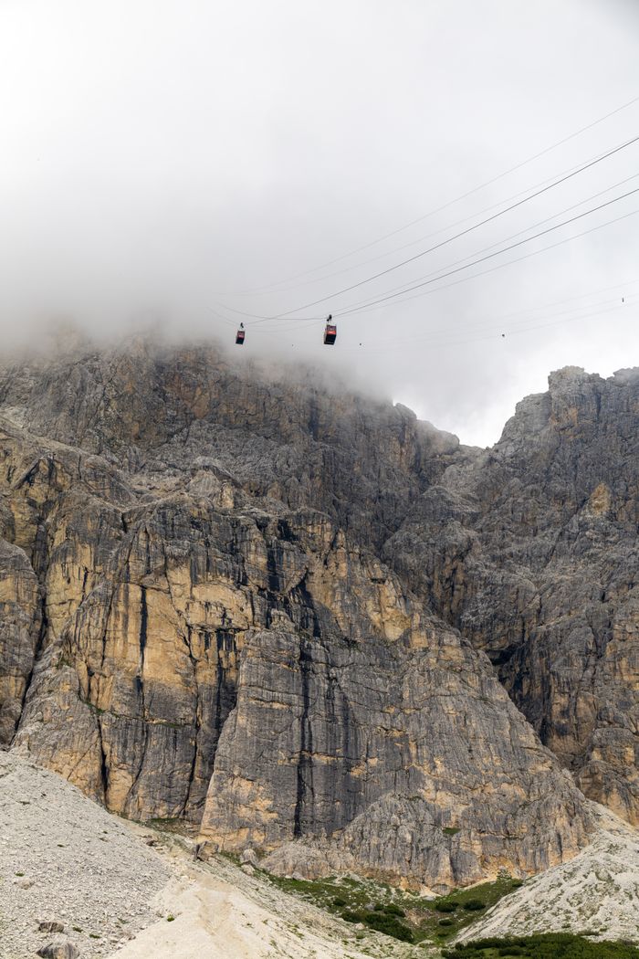Scenic view of gondola lift amidst fog and dramatic rock formations in the Dolomites.