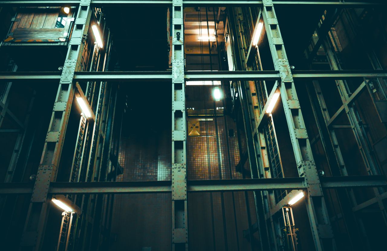 A dimly lit industrial elevator shaft with metal framework and lights.