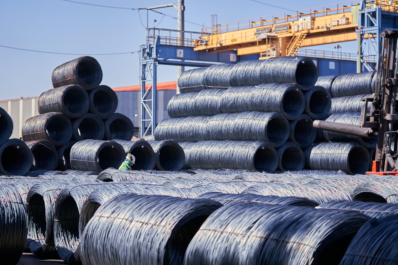 Large stacks of steel wire coils stored outdoors at an industrial site under bright daylight.
